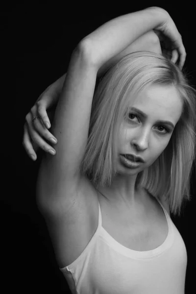 Black-and-white portrait of blonde in white T-shirt on a black background.