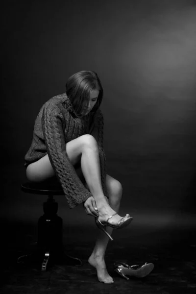 black and white portrait of an adult woman in a studio on a black background. sitting, buttoning her shoes