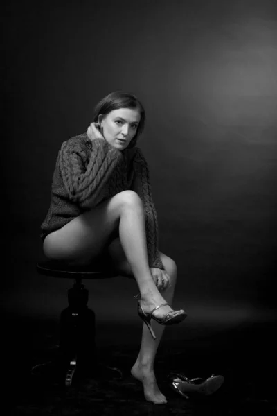 black and white portrait of an adult woman in a studio on a black background. sitting, buttoning her shoes
