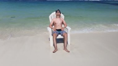 Kumsalda sandalyede dinlenen bir adam. Yaz tatili