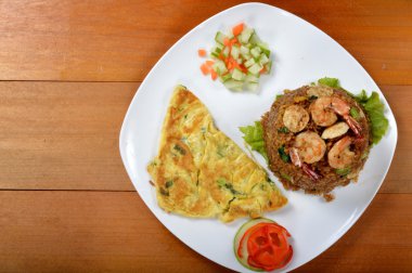 Tahta masadaki beyaz tabakta omletli kızarmış pirinç.