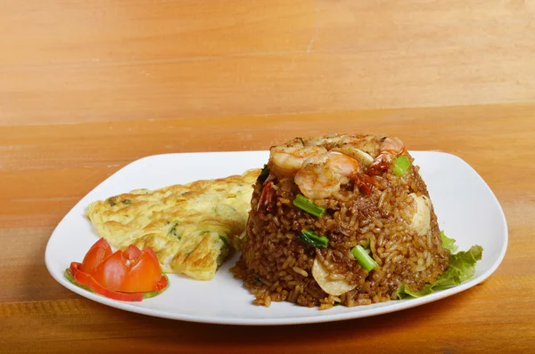 Жареный рис с омлетом на белой тарелке за деревянным столом — стоковое фото