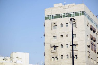 Çağdaş şehir yaşamını ve mimari tasarımı, berrak mavi gökyüzüne karşı modern kentsel yapı cephesini yansıtır. İş ve seyahat temaları için ideal.