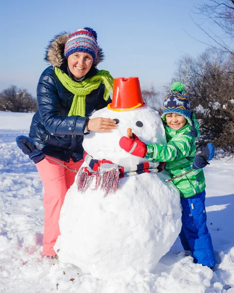 Jongen en zijn moeder met een sneeuwpop — Stockfoto