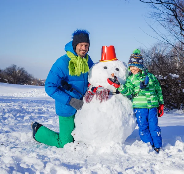 Мальчик и его отец со снеговиком — стоковое фото