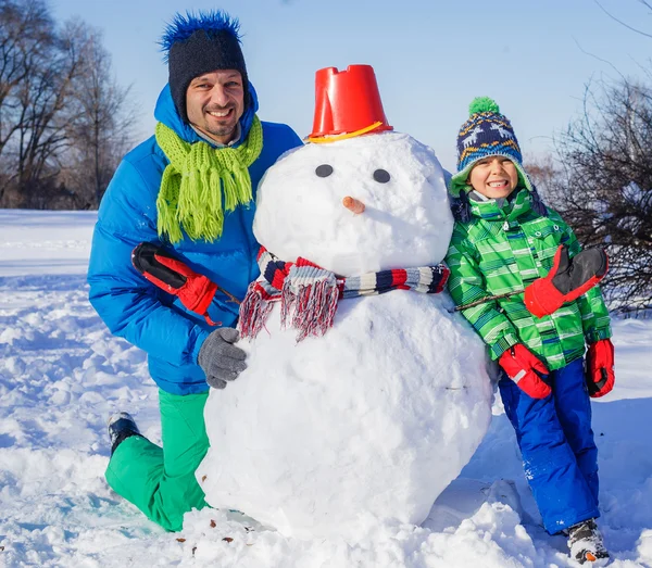 Niño y su padre con un muñeco de nieve — Foto de Stock