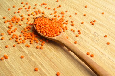 Kuru kırmızı ve turuncu mercimek tanecikleri tahta kaşıkta, bambu kesme tahtasında