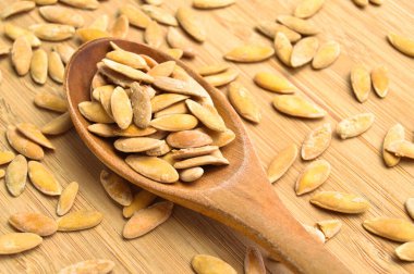 Kavrulmuş tuzlu organik kavun tohumları, bambu kesme tahtasının üzerinde ahşap kaşıkla.