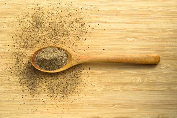 Ahşap bambu kesme tahtasının üzerinde kaşık içinde Aromatik ve taze kara biber tozu.