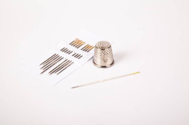 Dikiş dikmek için çelik dikiş iğnesi ve gümüş yüksük seti, beyaz arka planda izole.