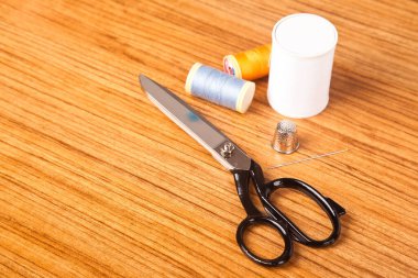 Dikiş malzemeleri konsepti, terzi makası renkli iplikler iğne ve yüksük, ahşap arka planda izole edilmiş.