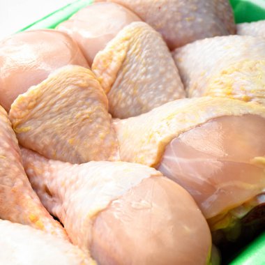 Taze pişmemiş tavuk budu parçaları, yeşil pakette pişmeye hazır bebek, beyaz arka planda.