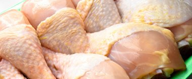 Taze pişmemiş tavuk budu parçaları, yeşil pakette pişmeye hazır bebek, beyaz arka planda.
