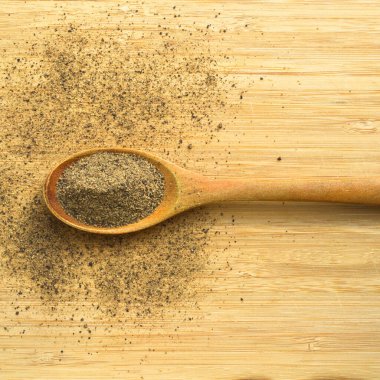 Ahşap bambu kesme tahtasının üzerinde kaşık içinde Aromatik ve taze kara biber tozu.