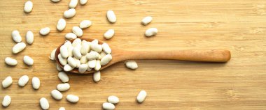 Kurumuş organik fasulyeler bambu kesme tahtasının üzerinde tahta kaşıkta.