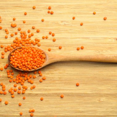 Kuru kırmızı ve turuncu mercimek tanecikleri tahta kaşıkta, bambu kesme tahtasında