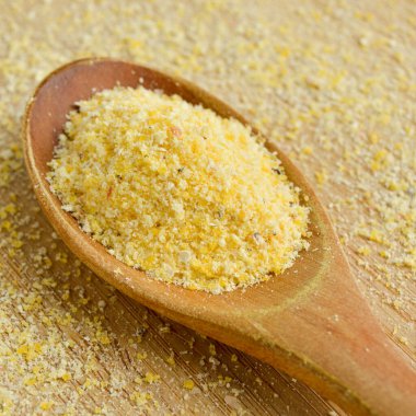 Tahta kesme tahtasındaki ahşap kaşıkta pişmemiş sarı mısır unu.