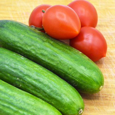 Tahtada taze ve sağlıklı yeşil salatalık ve domates var.