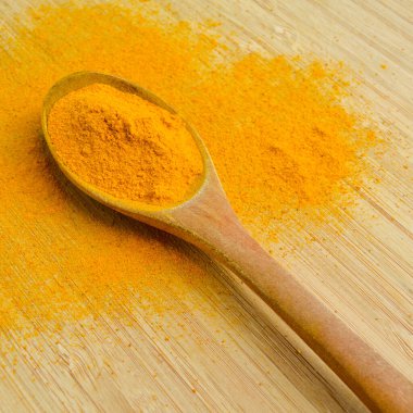 Bambu ahşap arka planda ahşap kaşıkta taze zerdeçal tozu.
