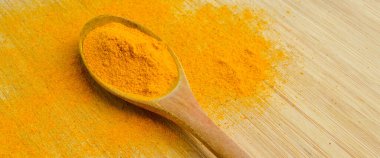 Bambu ahşap arka planda ahşap kaşıkta taze zerdeçal tozu.