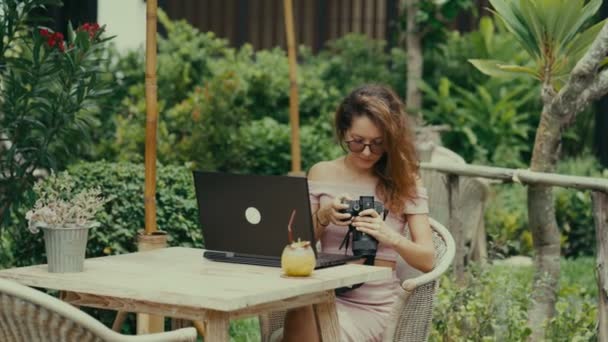Een jonge vrouw fotograaf werken met haar laptop in een outdoor cafe — Stockvideo