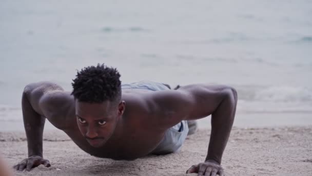 Sahilde egzersiz yaparken şınav çeken Afrikalı Amerikalı bir adam. — Stok video