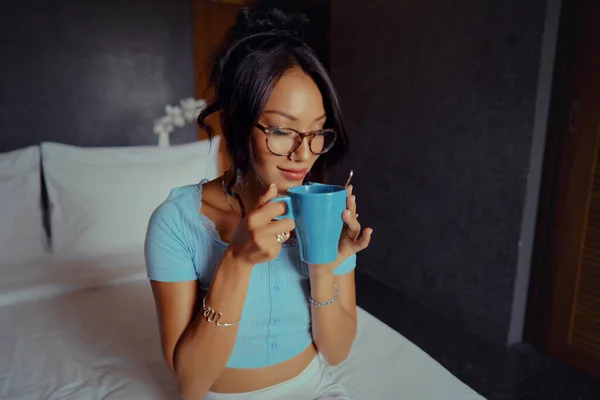 Bella donna asiatica che tiene e beve caffè sul letto al mattino — Foto Stock