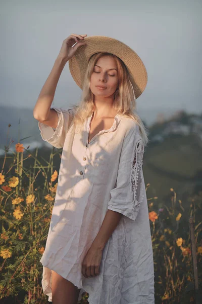 Blondynka w lnianej sukience spaceruje wśród ziół i dzikich kwiatów na łące w górach — Zdjęcie stockowe