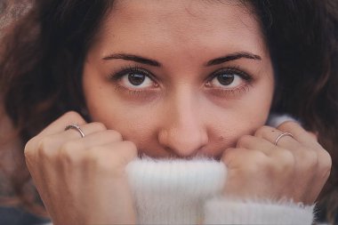 Genç bir kadın beyaz kazağını kafasına geçiriyor.