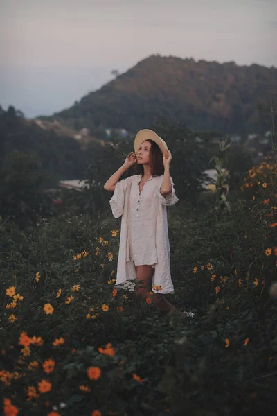 Keten elbiseli ve hasır şapkalı genç bir kadın dağlarda bir bakış açısında oturuyor. — Stok fotoğraf