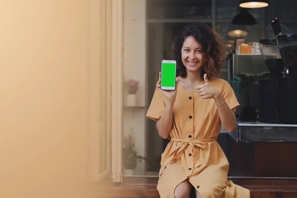 Uma mulher segurando e mostrando telefone celular com tela verde em branco no café — Fotografia de Stock