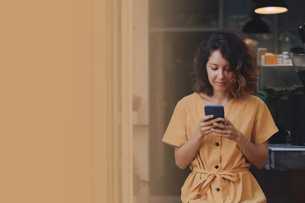 Jovem mulher usando vestido amarelo usando seu telefone inteligente no terraço da cafetaria — Fotografia de Stock