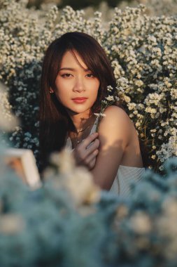 Güzel Asyalı kadın beyaz elbise giyer, beyaz kesme çiçeklerle dolu bahçede yürür.