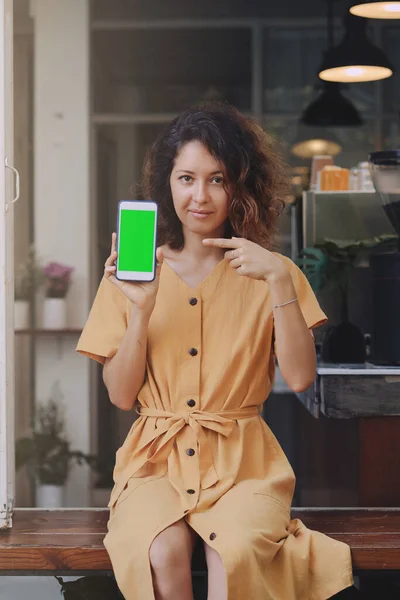 Uma mulher segurando e mostrando telefone celular com tela verde em branco no café — Fotografia de Stock