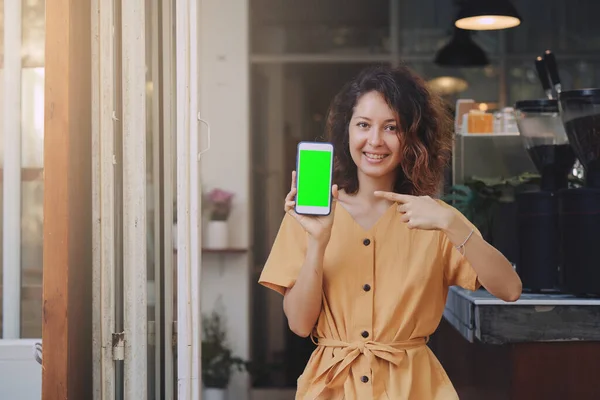 Uma mulher segurando e mostrando telefone celular com tela verde em branco no café — Fotografia de Stock