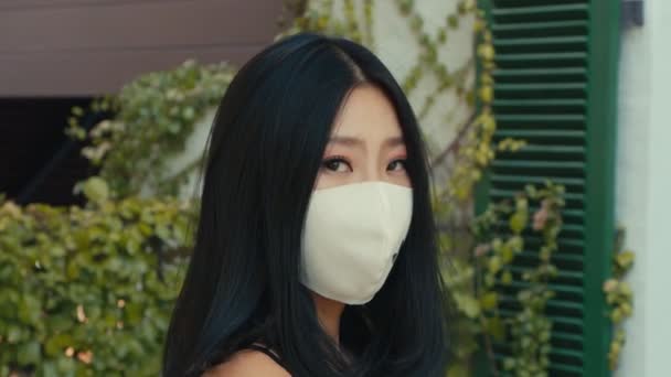 Eine junge Asiatin trägt eine medizinische Maske und blickt auf der Straße direkt in die Kamera — Stockvideo