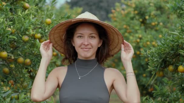 Girl standing and smiling in an orange orchard wearing a vietnamese hat looking straight at the camera — Stock Video