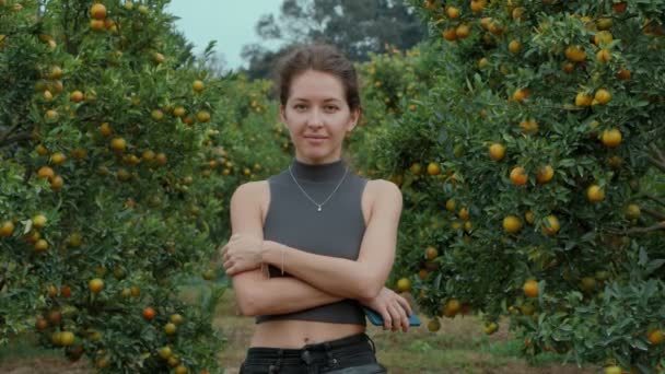 Chica de pie y sonriendo en un huerto naranja mirando directamente a la cámara — Vídeo de stock