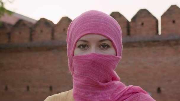Atractiva mujer musulmana con maquillaje natural usando bufanda hijab rosa mira a la cámara — Vídeo de stock