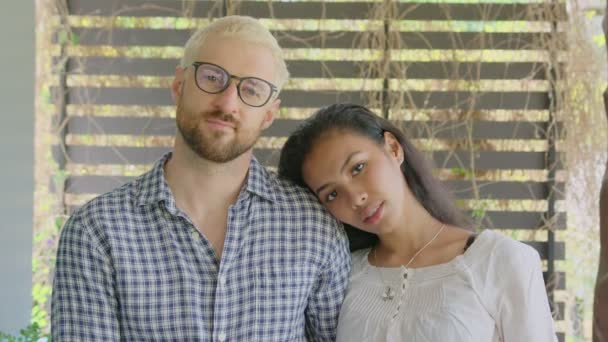 Un jeune couple interracial international amoureux regarde droit devant la caméra par une journée ensoleillée au jardin de la maison — Video