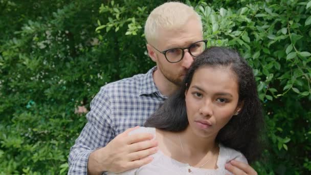 Ein junges internationales gemischtes verliebtes Paar blickt an einem sonnigen Tag im heimischen Garten direkt in die Kamera — Stockvideo