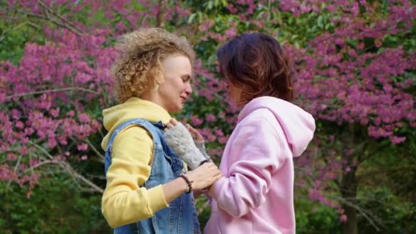 Pareja lesbiana homosexual abrazándose en un jardín de sakura. Dos mujeres comparten amor y apoyo mientras se toman de la mano. Familia Gay. Concepto LGBT de amistad — Vídeos de Stock