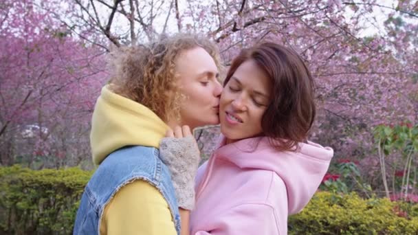 Pareja de lesbianas abrazándose en un jardín de sakura. Dos mujeres comparten amor y apoyo mientras se toman de la mano. Familia Gay. Concepto LGBT de amistad — Vídeos de Stock