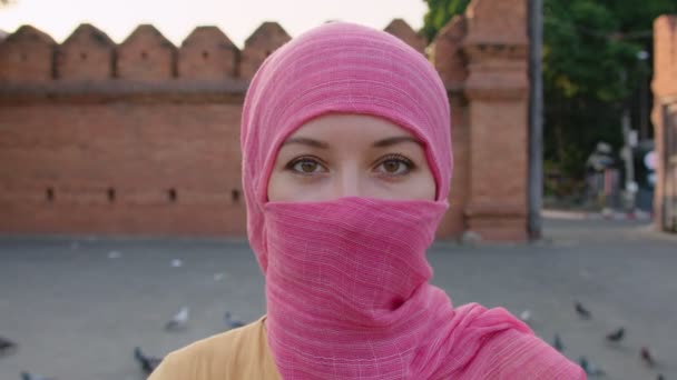 Doğal makyajlı, pembe başörtüsü takan çekici Müslüman kadın kameraya bakıyor. — Stok video