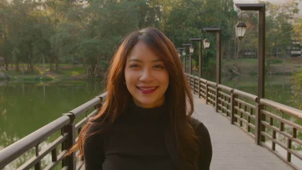 Retrato de uma bela mulher tailandesa em uma ponte no parque ao pôr do sol — Vídeo de Stock