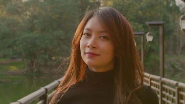 Retrato de uma bela mulher tailandesa em uma ponte no parque ao pôr do sol — Vídeo de Stock