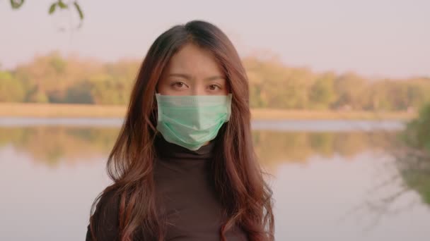 Портрет счастливой тайской молодой женщины в защитной маске, стоящей в парке на закате — стоковое видео