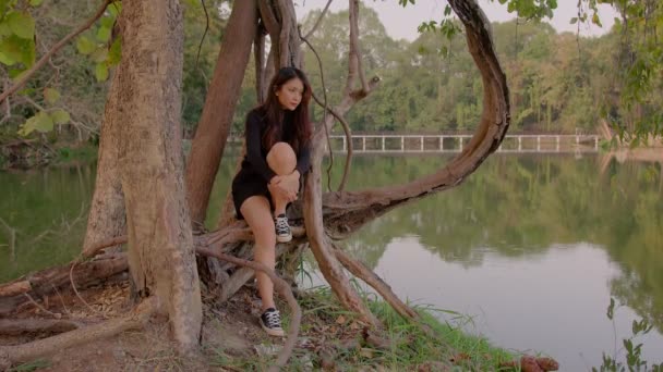 Thaise jonge vrouw zit gepensioneerd door meer in park bij zonsondergang — Stockvideo