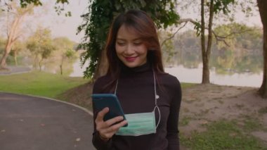 Güneş batarken parkta duran koruyucu yüz maskesi takan mutlu Taylandlı genç kadının portresi.