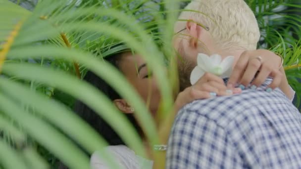 Молодая международная межрасовая пара влюблена и целуется в солнечный день в домашнем саду — стоковое видео